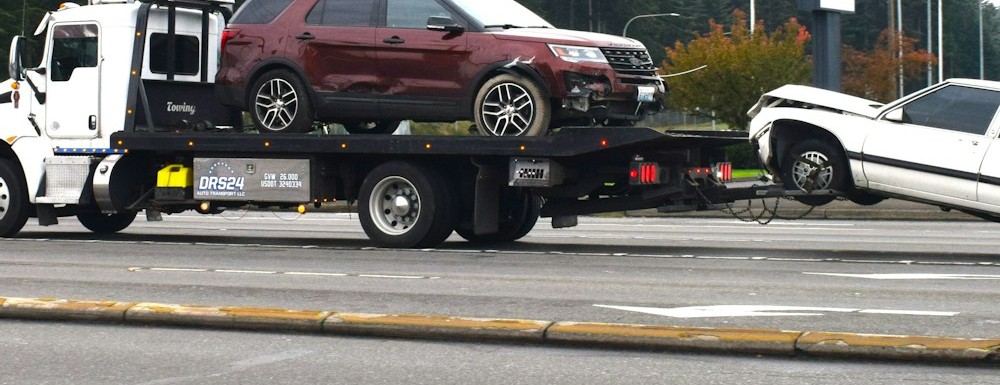 Flatbed tow truck carrying a collision-damaged SUV